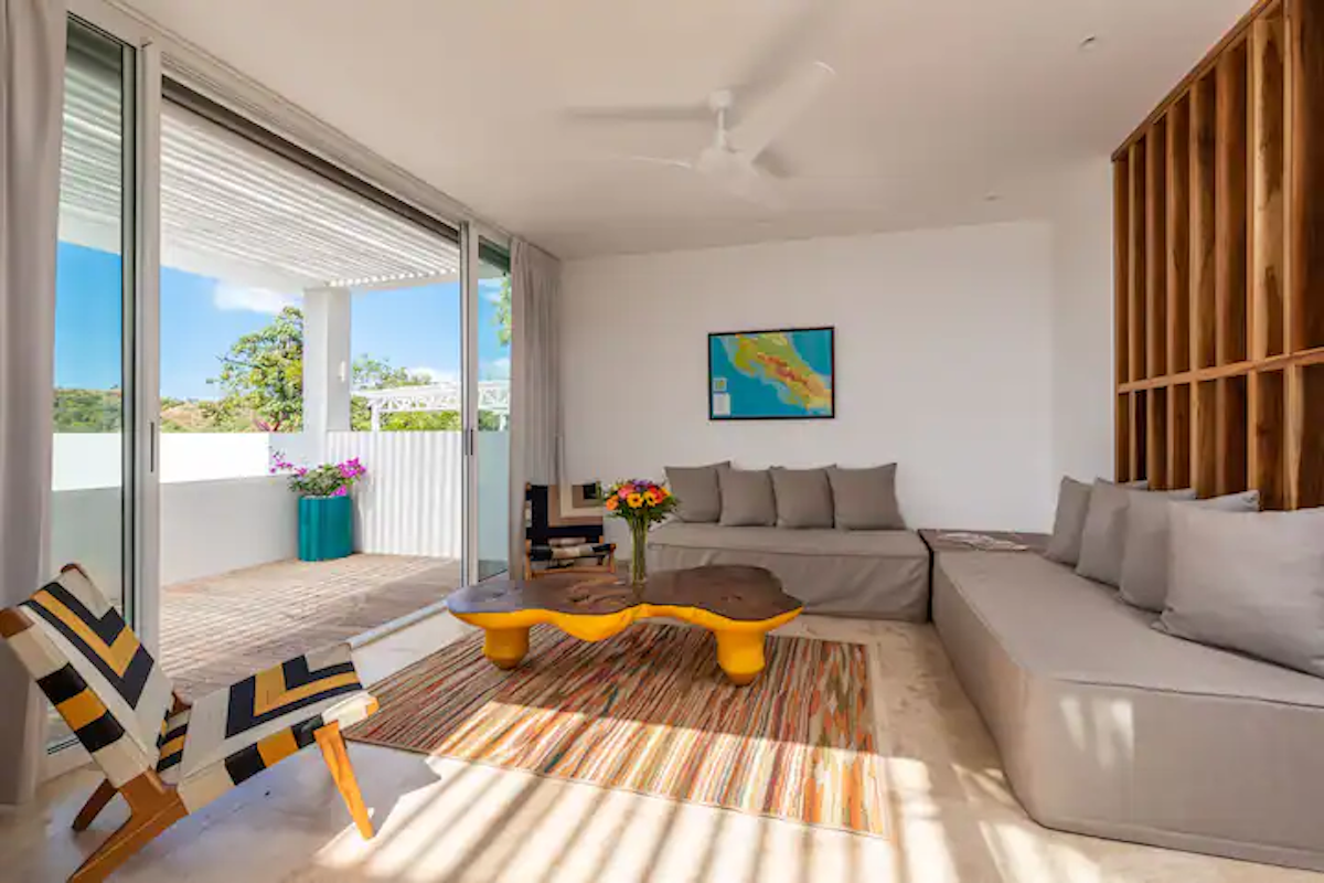 Salon lumineux avec portes coulissantes, canapé gris pâle, table basse jaune et tapis.