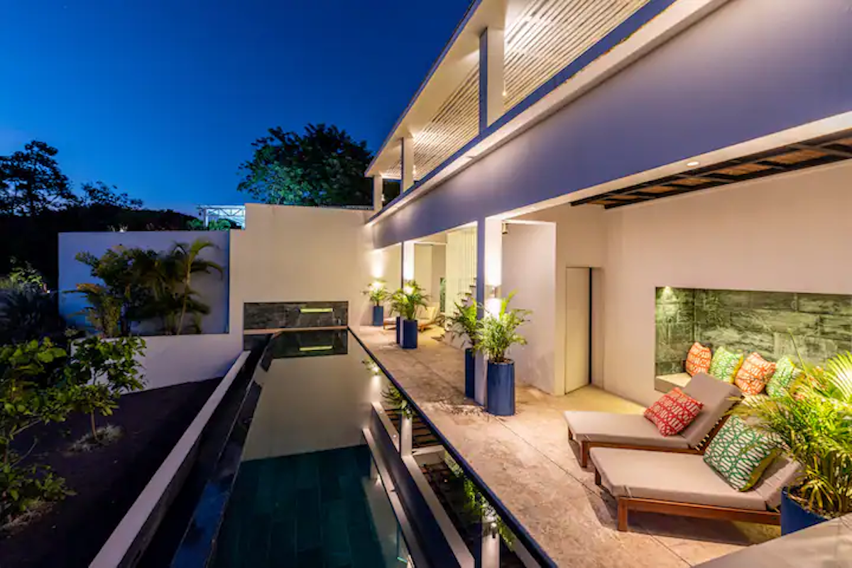 Villa de luxe au crépuscule avec piscine, chaises longues et patio éclairé.