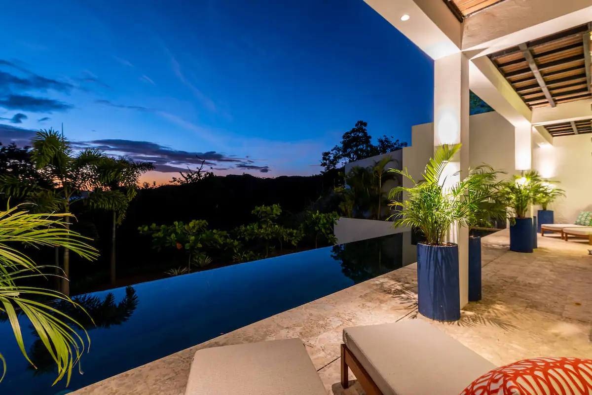 Vue nocturne d'une piscine à débordement surplombant les montagnes ; des chaises longues et un coin salon sont à proximité.