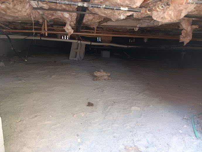 A very dirty basement with a lot of insulation and pipes.