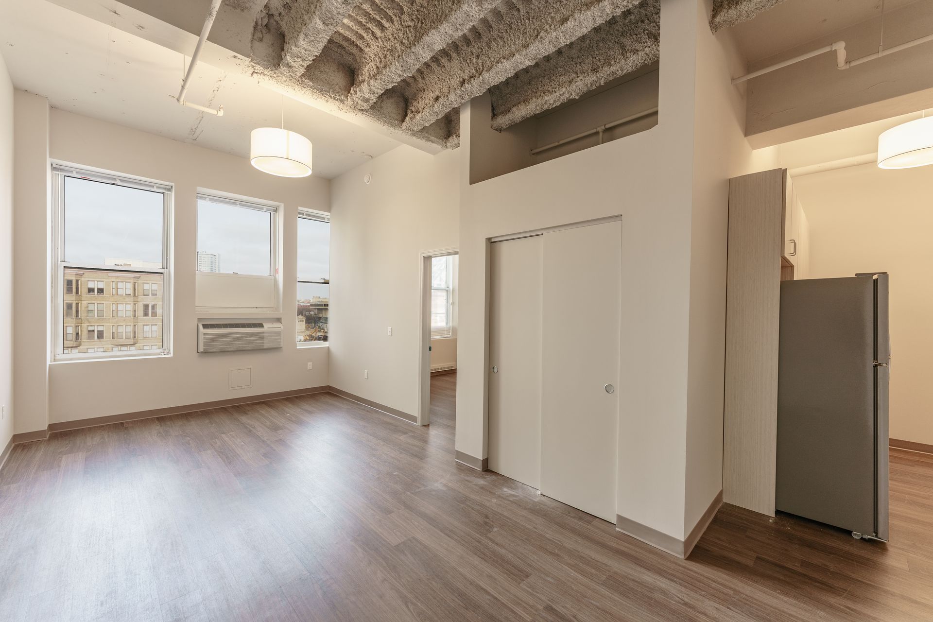 An empty living room with hardwood floors and a refrigerator.