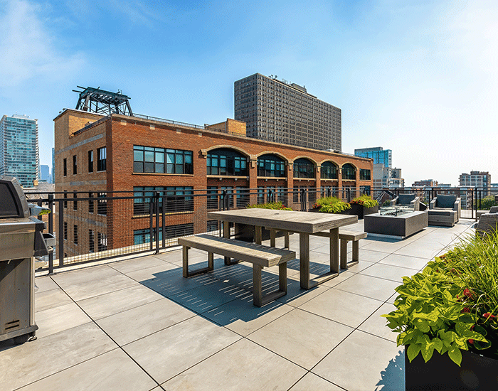 There is a picnic table and a grill on the roof of a building.