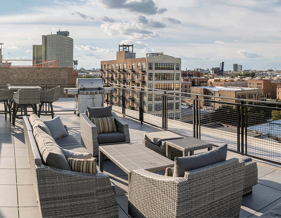 A rooftop patio with a couch , chairs , table and grill.