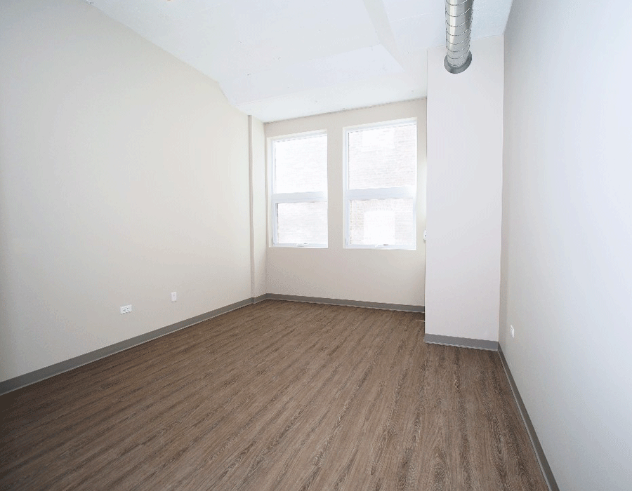 An empty room with hardwood floors and two windows.
