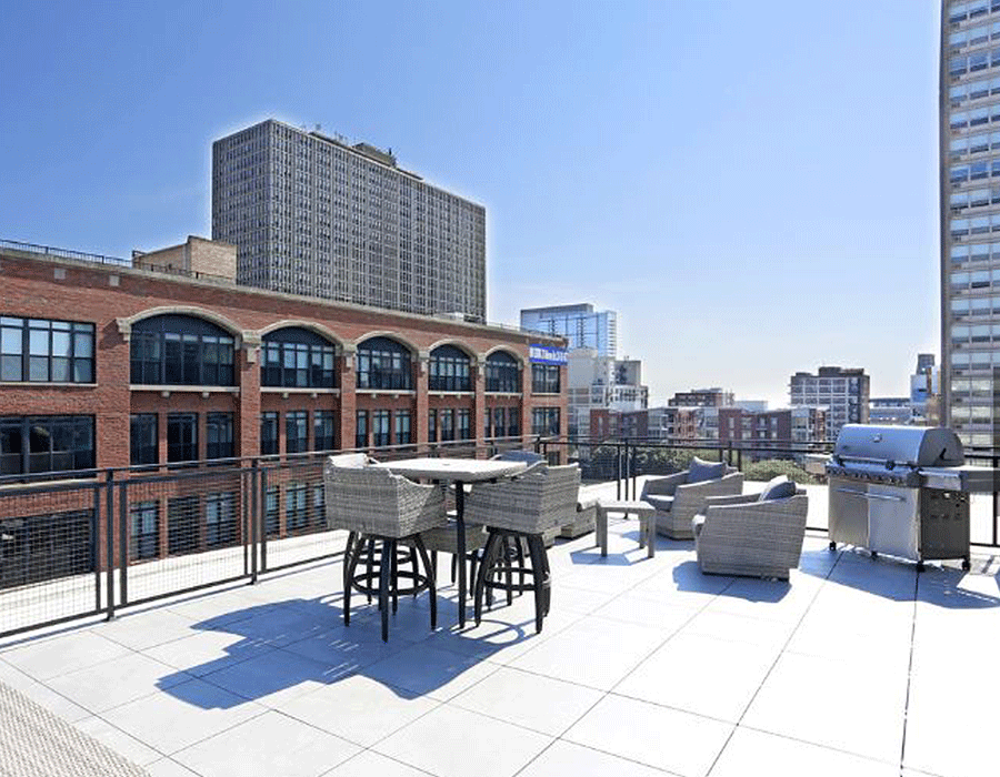 A rooftop deck with a table and chairs and a grill.