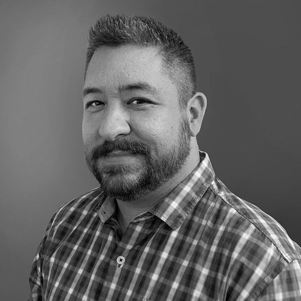 A black and white photo of a man with a beard wearing a plaid shirt.
