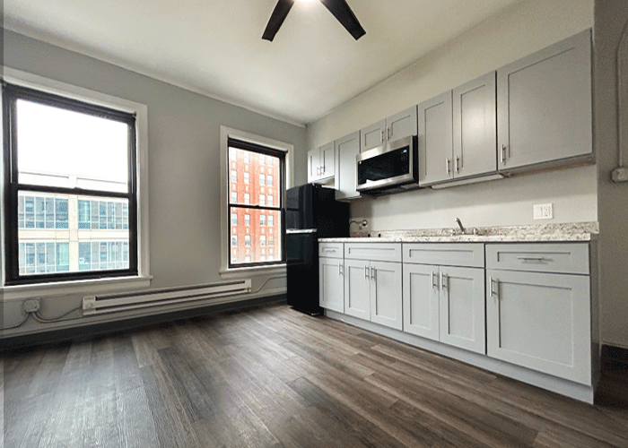 A kitchen with white cabinets , a black refrigerator , a microwave , and a ceiling fan.