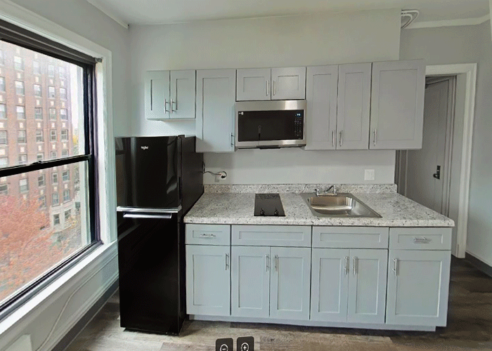 A kitchen with white cabinets , a black refrigerator , a sink , and a window.