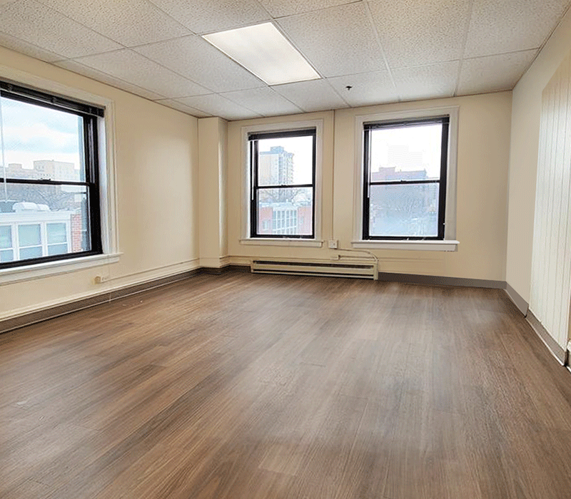 An empty room with hardwood floors and two windows.