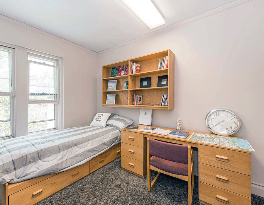 A bedroom with a bed , desk , chair and clock.