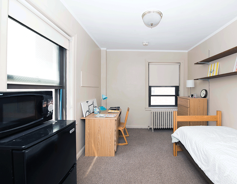 A bedroom with a bed a desk and a microwave