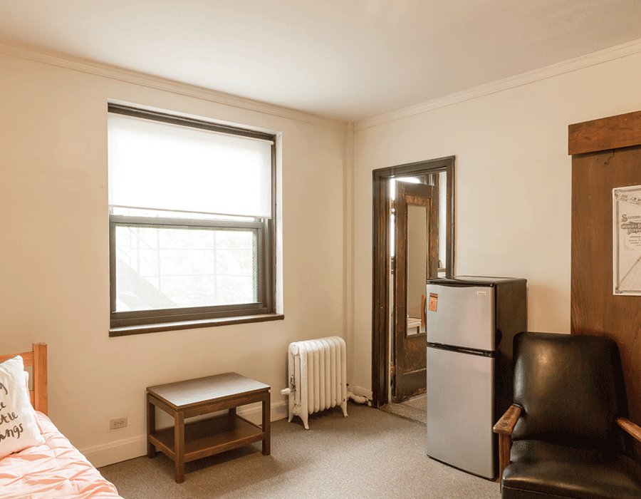 A bedroom with a bed , chair , table and refrigerator.