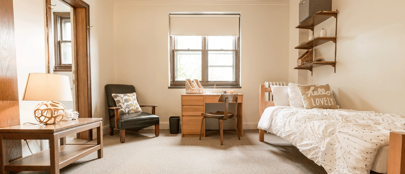 A bedroom with a bed , desk , chair and lamp.