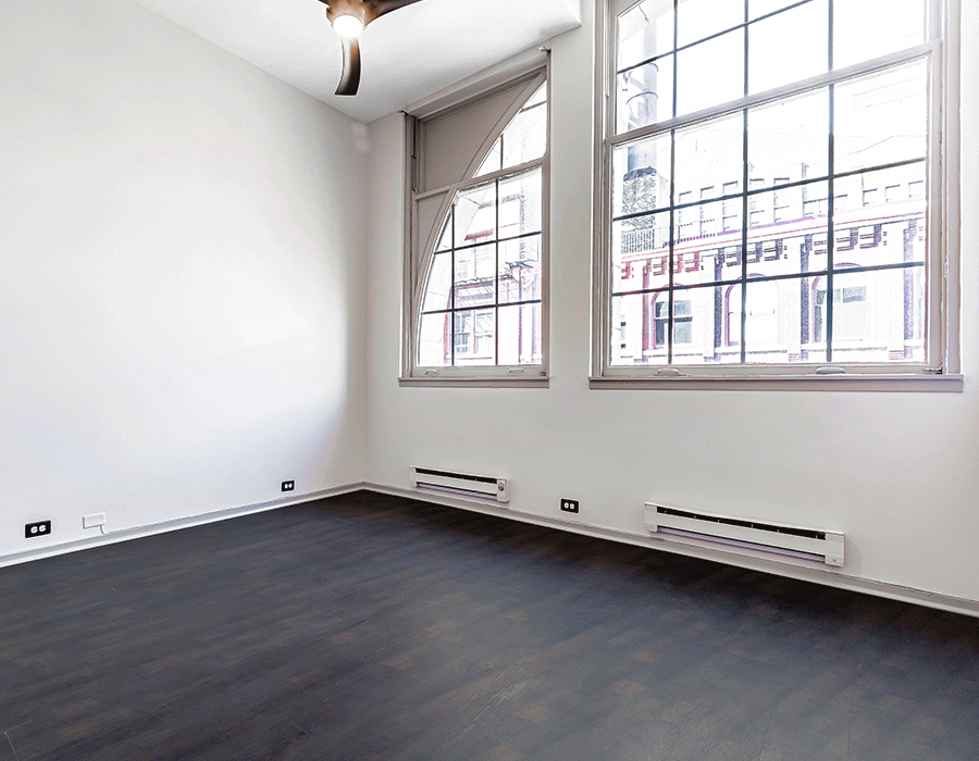 An empty room with a lot of windows and a ceiling fan.