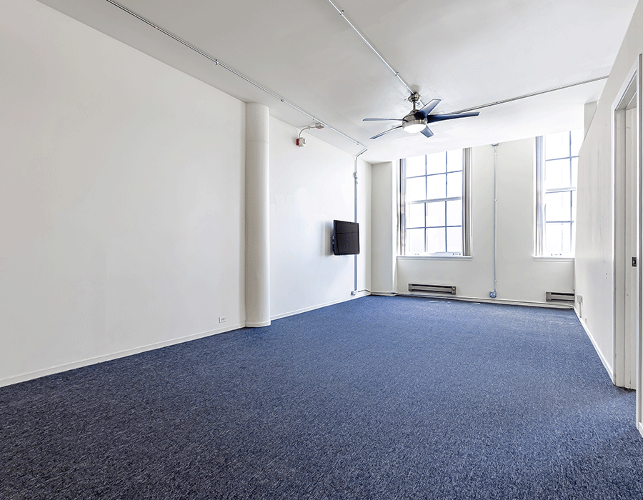 An empty room with blue carpet and a ceiling fan.