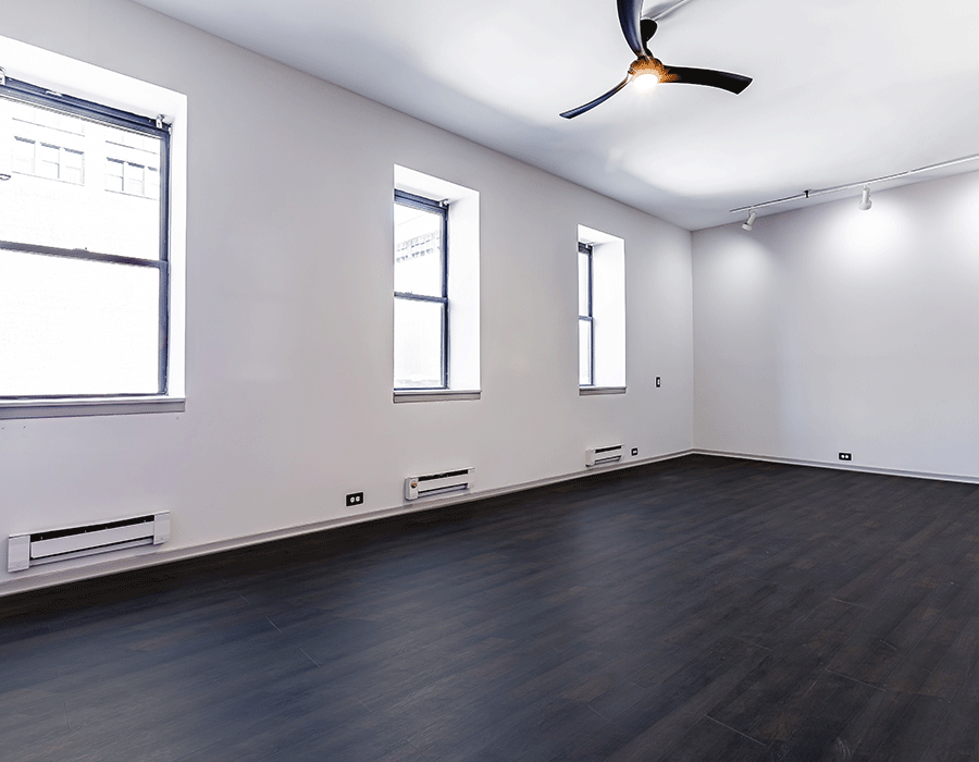 An empty room with a ceiling fan and three windows