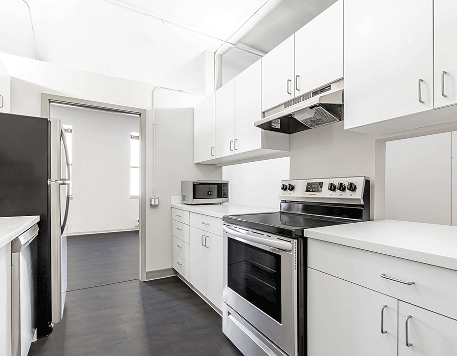 A kitchen with white cabinets , a stove , a refrigerator , and a microwave.