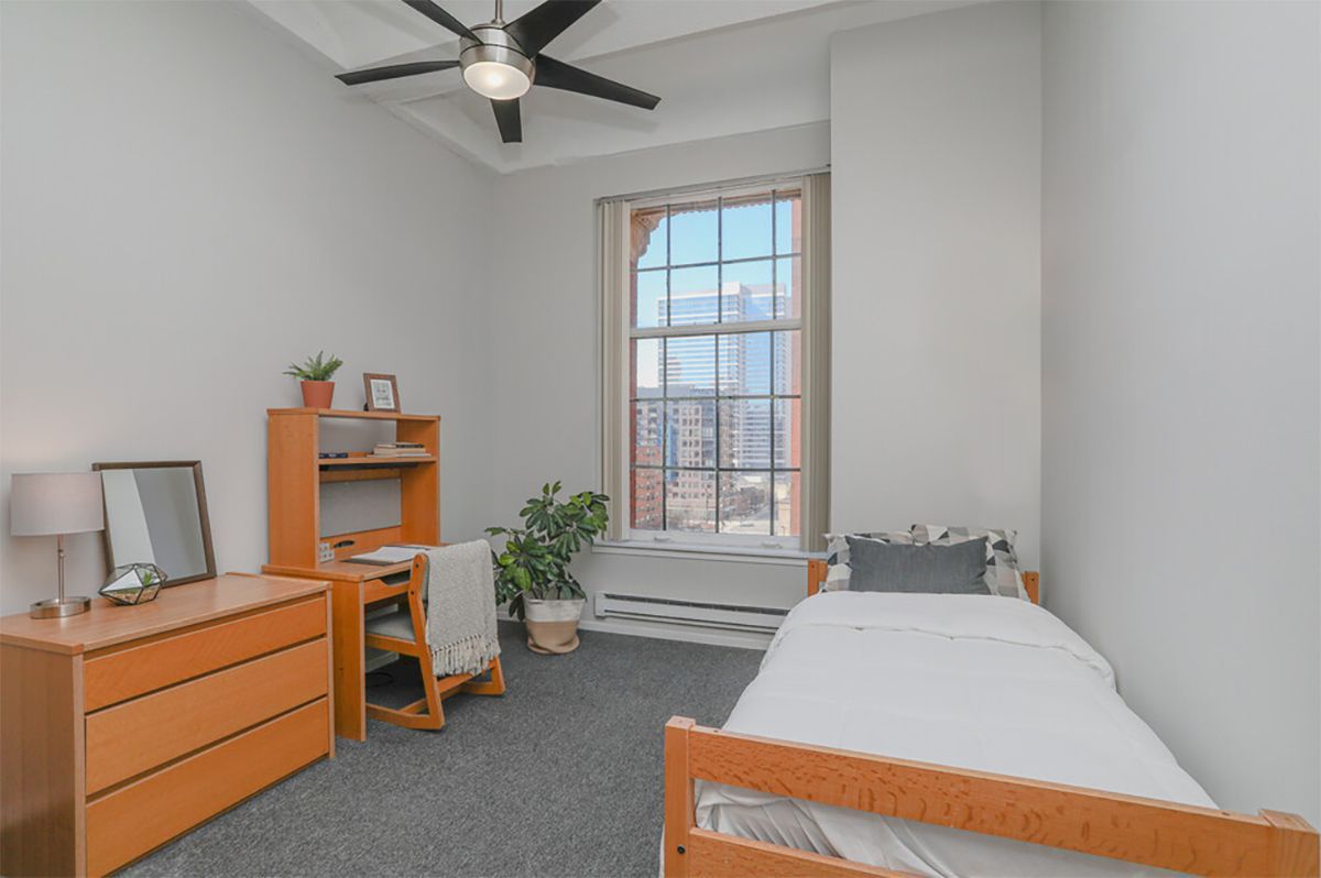 A bedroom with a single bed , desk , dresser and ceiling fan.