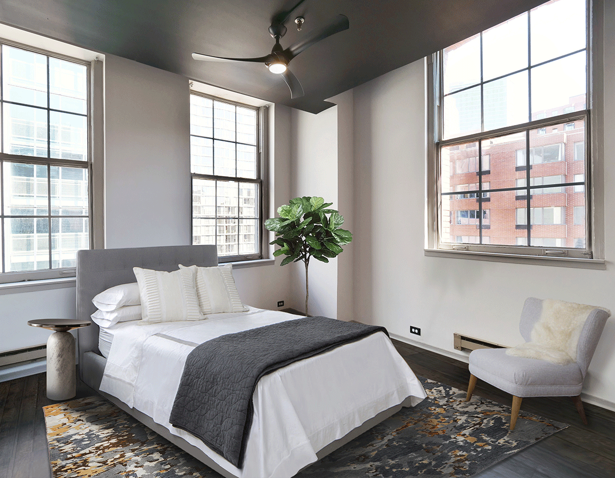 A bedroom with a bed , chair and ceiling fan.