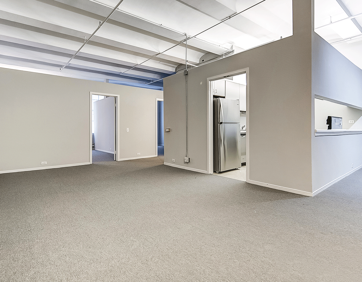 An empty room with a carpeted floor and a refrigerator
