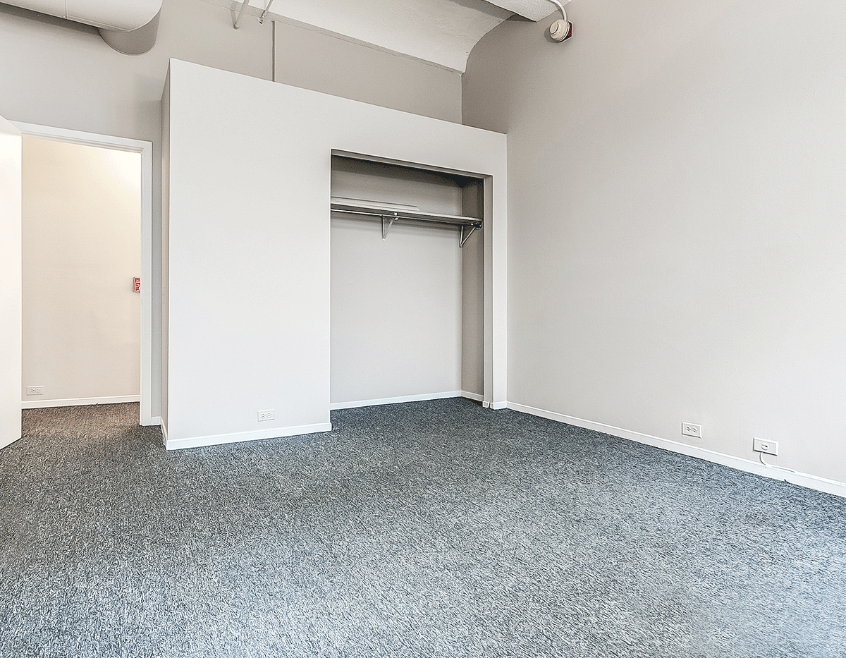 An empty room with a gray carpet and a closet.