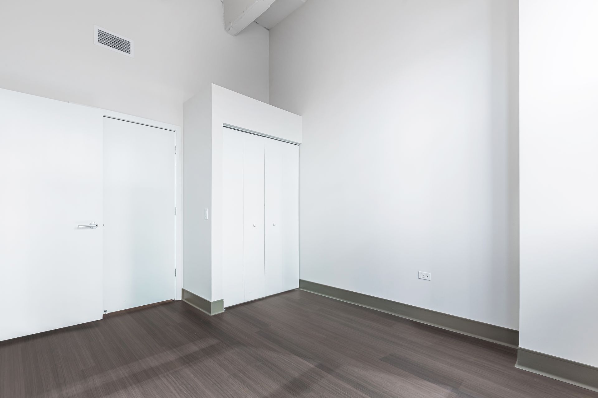 An empty bedroom with hardwood floors and white walls