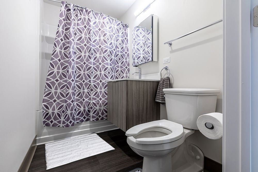 A bathroom with a toilet , sink , shower and purple shower curtain.