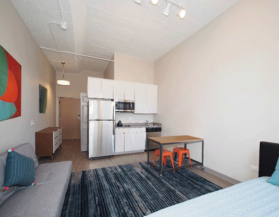 A bedroom with a couch , table , refrigerator and microwave.