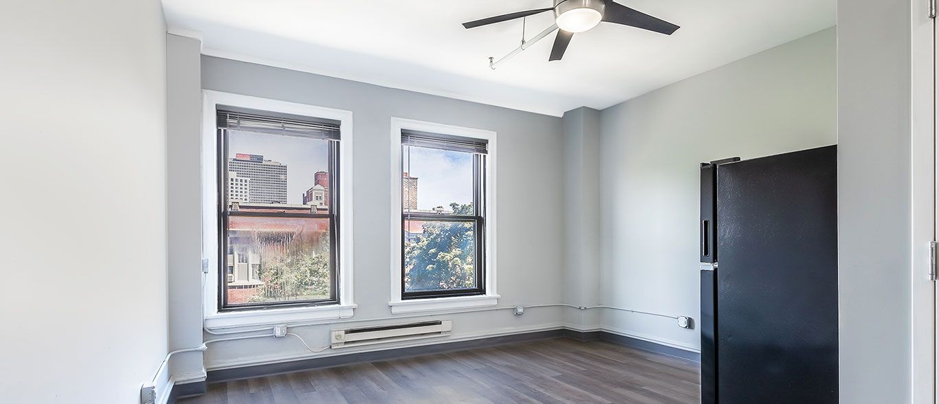 An empty room with a black refrigerator and a ceiling fan.