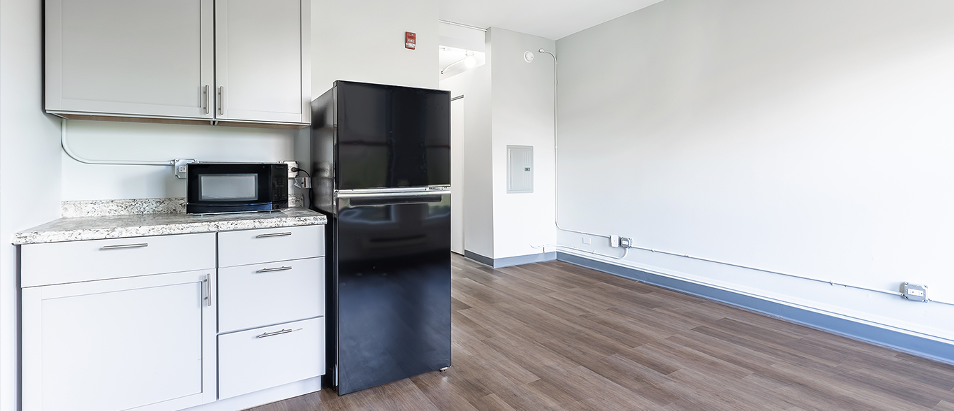 A kitchen with white cabinets , a black refrigerator and a microwave.