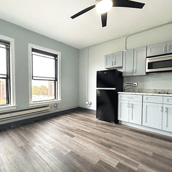 A kitchen with white cabinets , a black refrigerator , a microwave , and a ceiling fan.