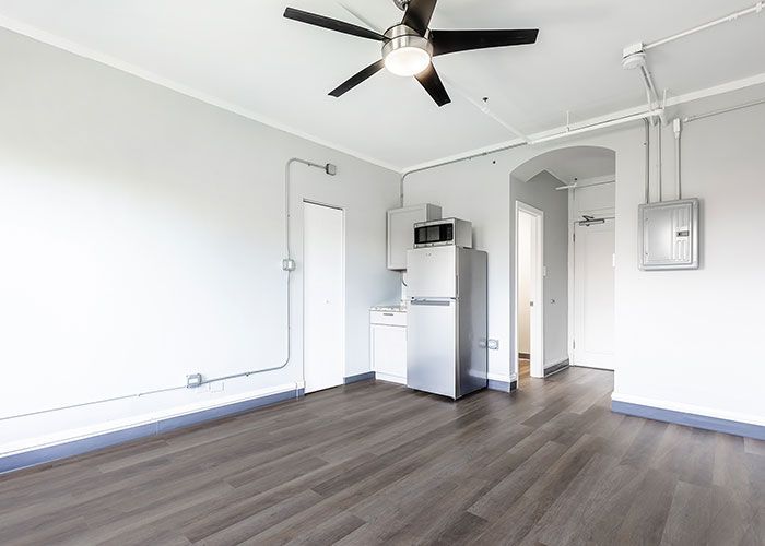 An empty room with a ceiling fan and a refrigerator.