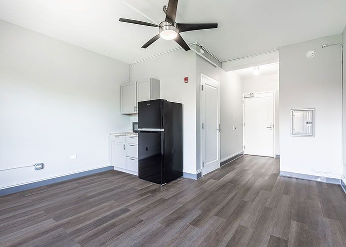 A living room with a black refrigerator and a ceiling fan.