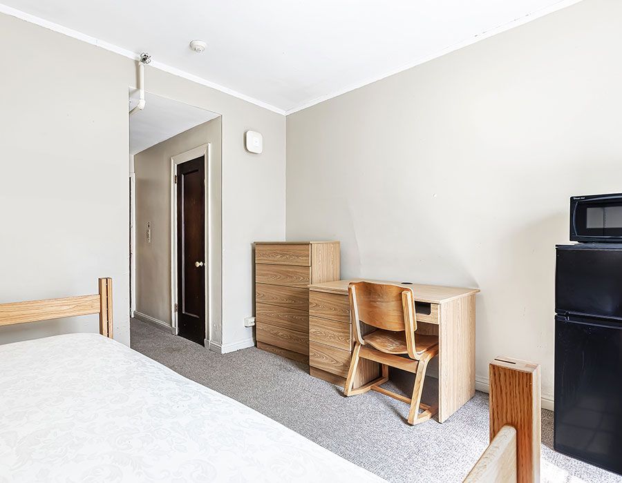 A bedroom with a bed , desk , chair and refrigerator.
