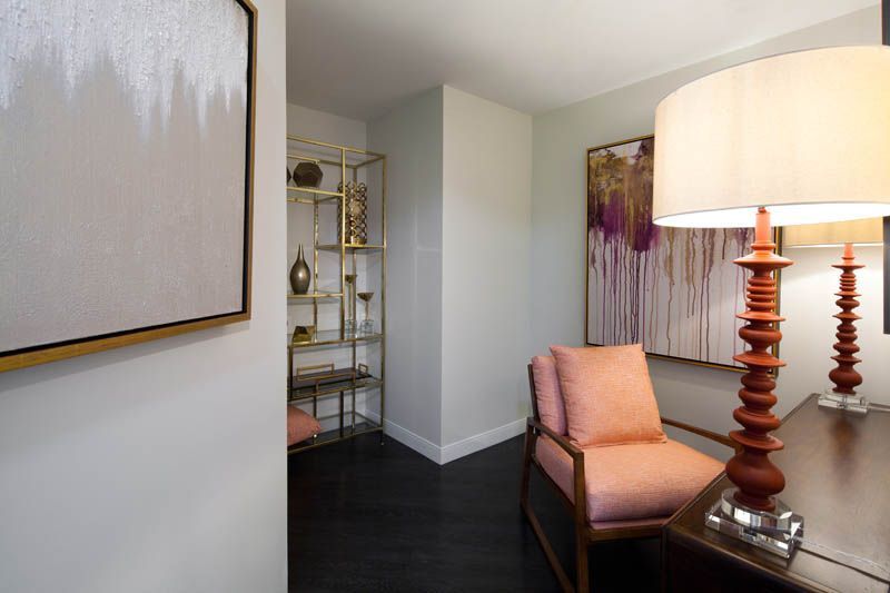 A living room with a chair , desk , lamps and a painting on the wall.