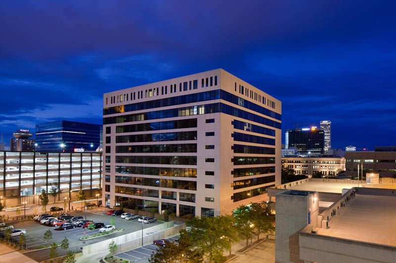 An aerial view of a large building with a parking garage in the background at night.