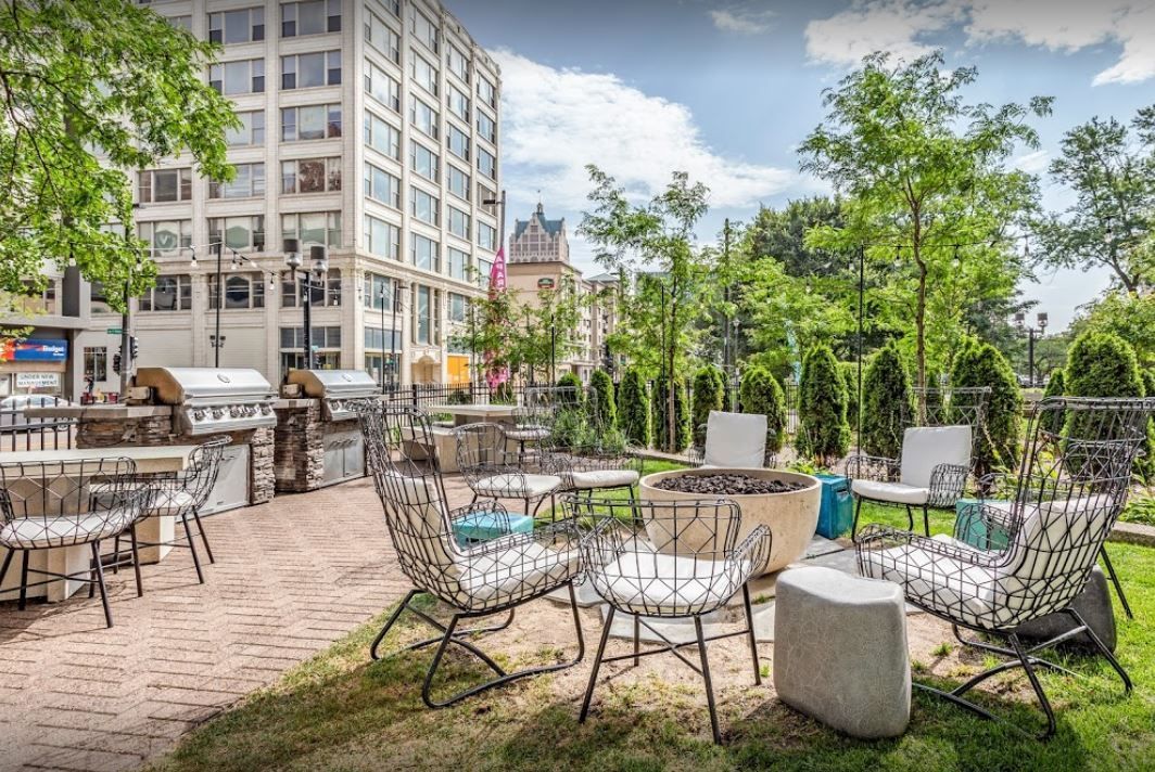 A patio with a fire pit and chairs in front of a building.