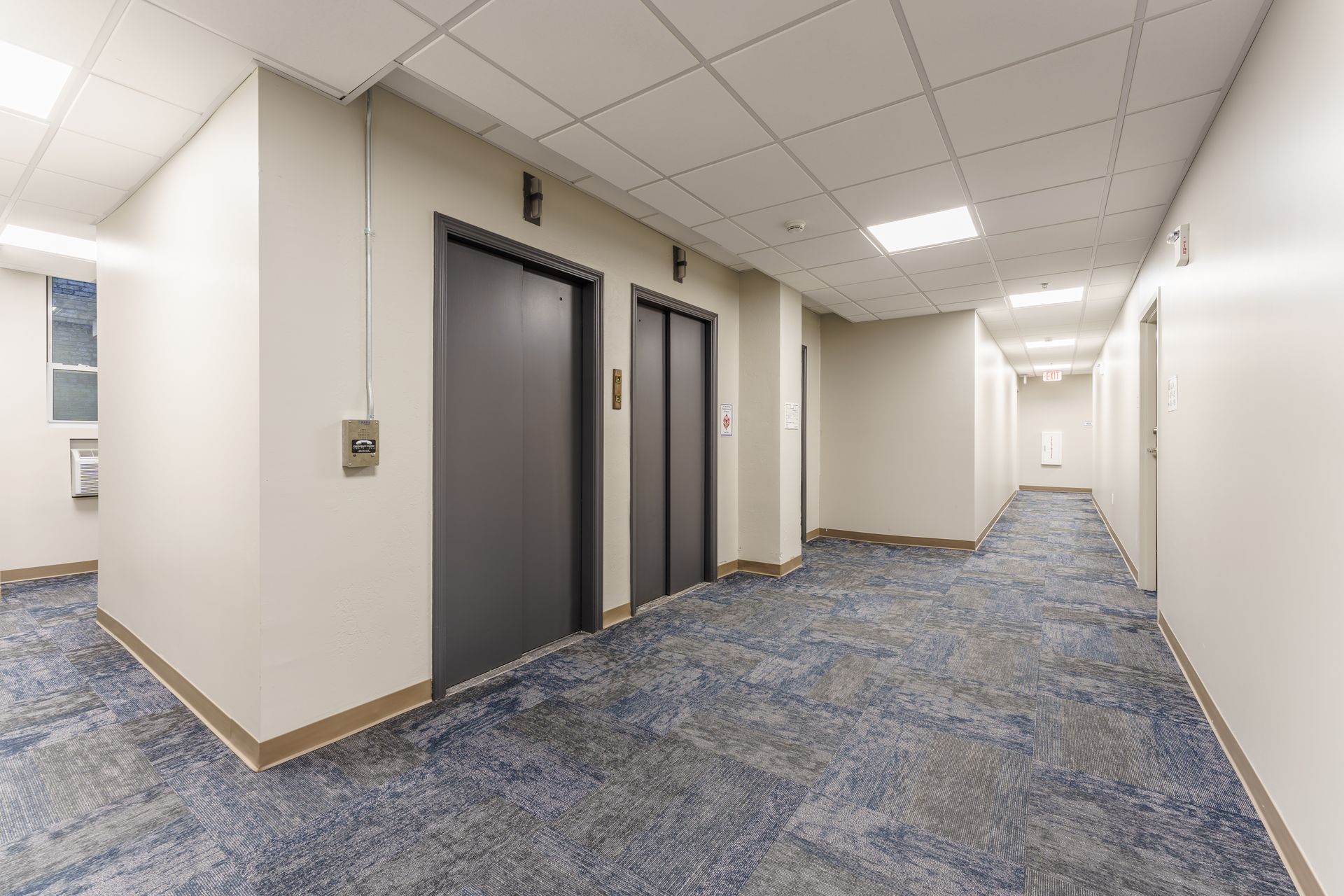 A long hallway with two elevators in a building.
