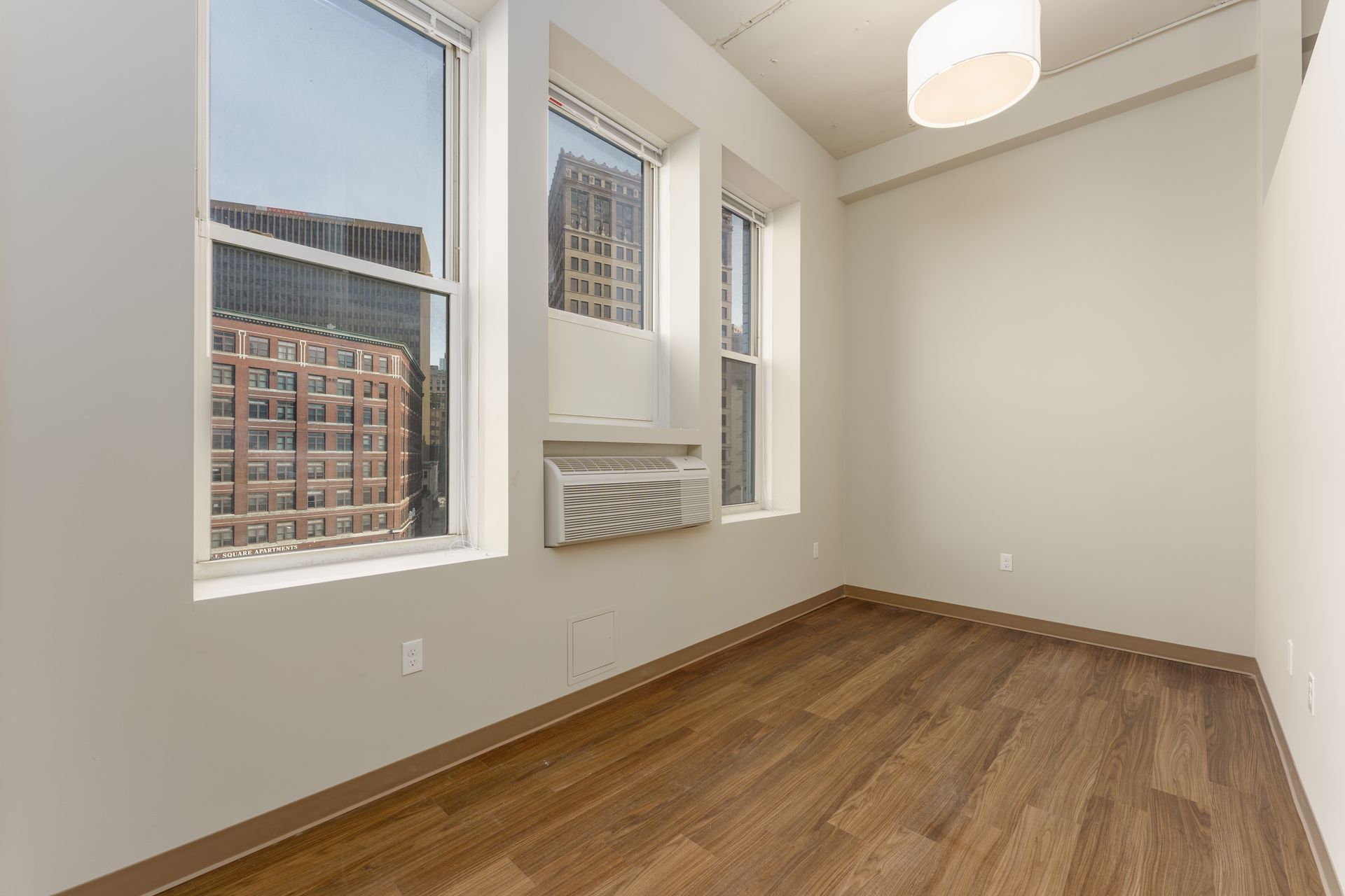 An empty room with hardwood floors and three windows.