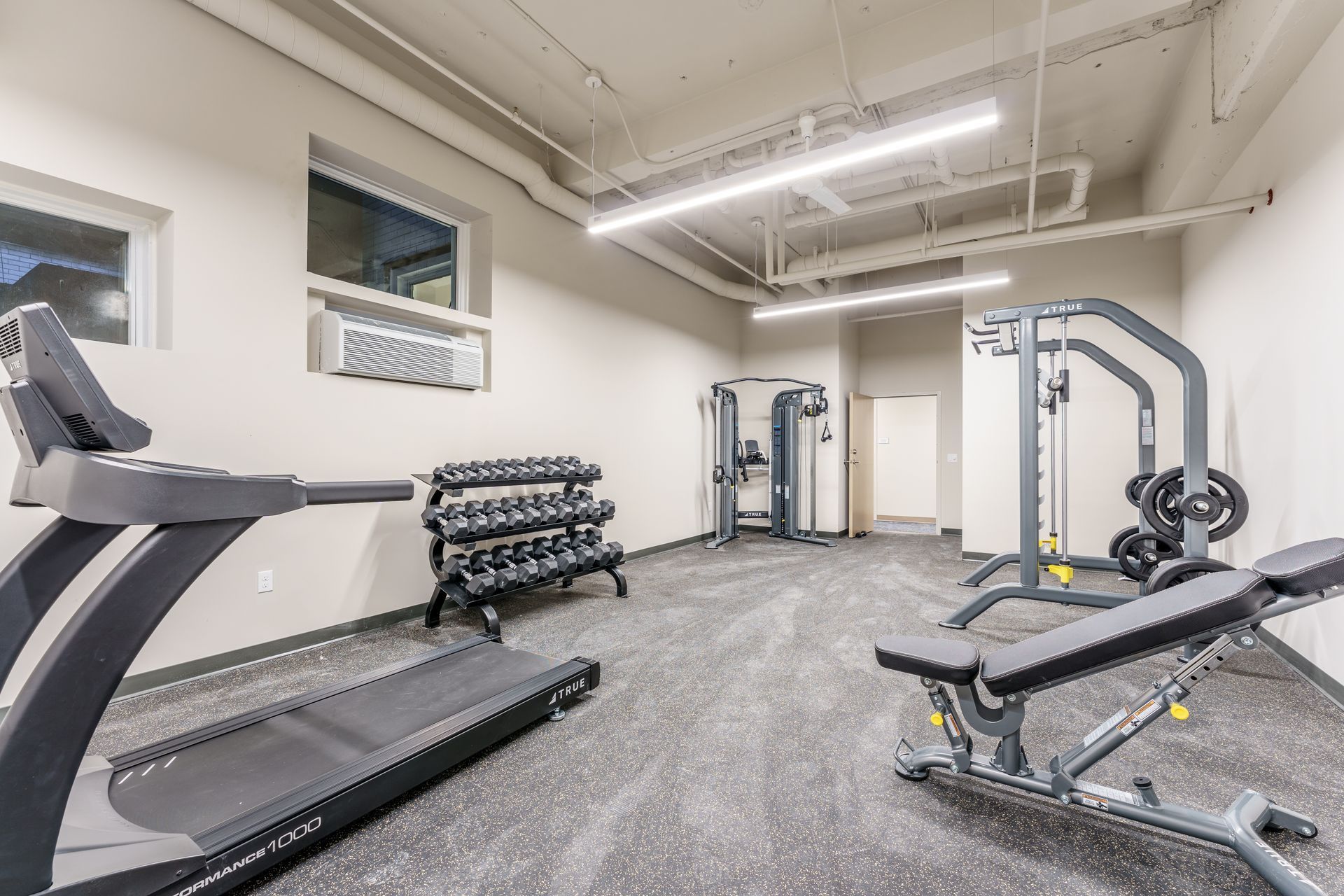 A gym with a treadmill , dumbbells , and a bench.