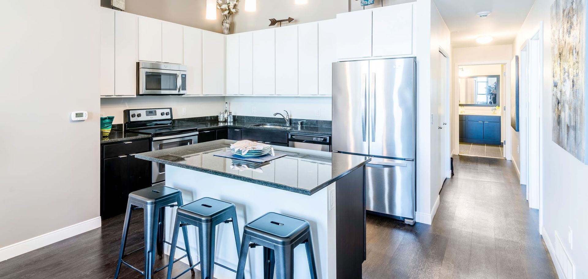 A kitchen with white cabinets , stainless steel appliances , a large island and stools.
