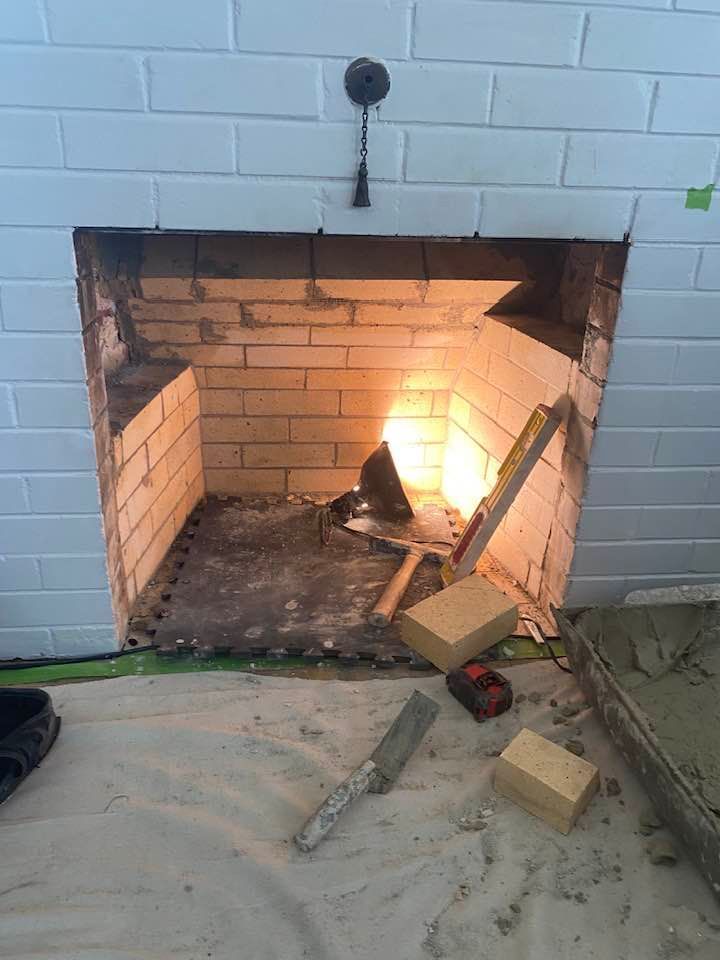 Fireplace interior with brickwork, tools, and a bright light. White tiled surround.
