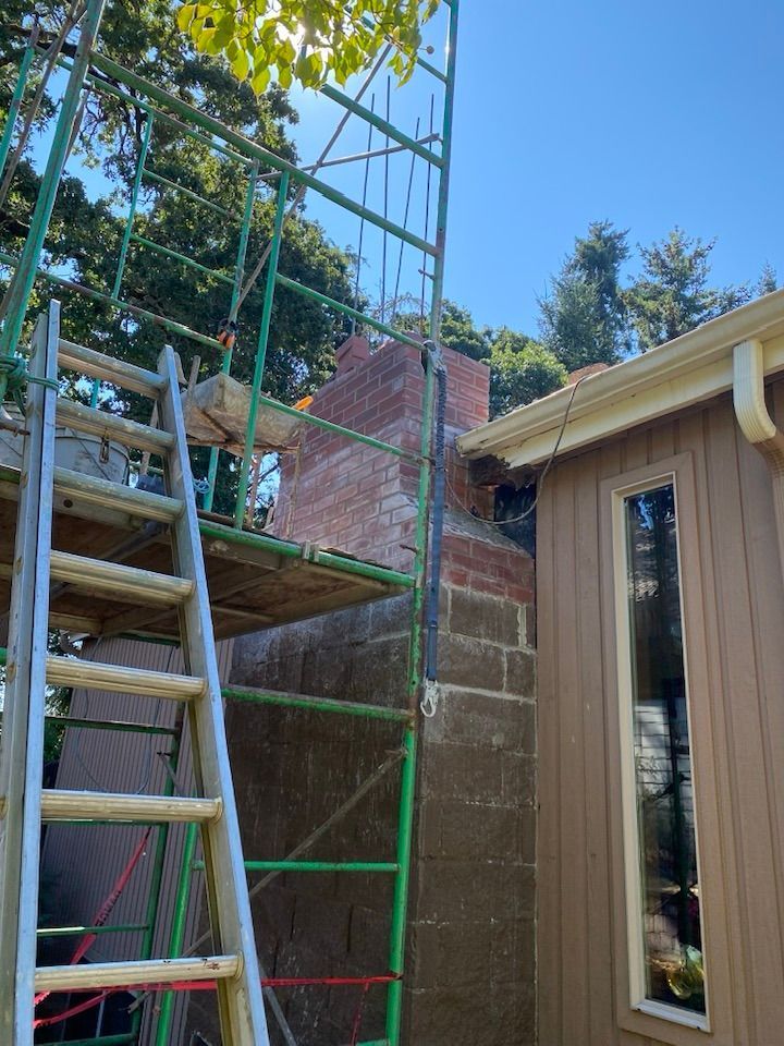 Chimney repair with scaffolding and ladder next to a brown house under a blue sky.