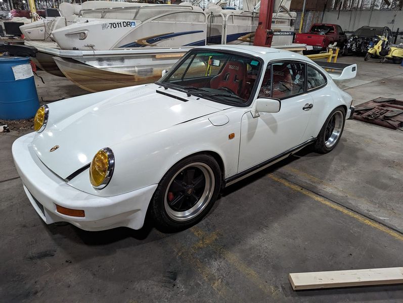 A white porsche is parked in a garage next to boats.