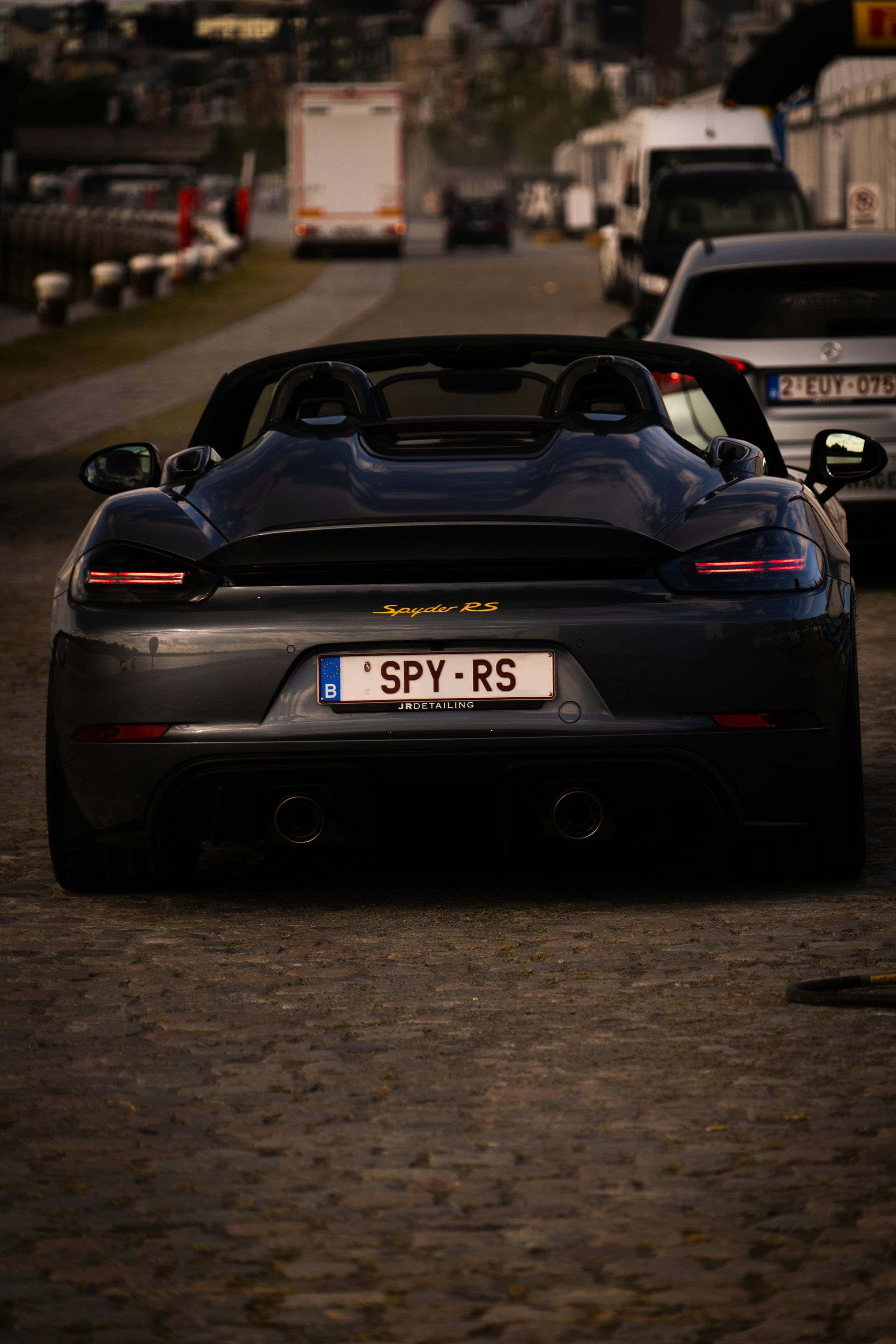 Dark gray Porsche Boxster, rear view, on a road, with a license plate reading 