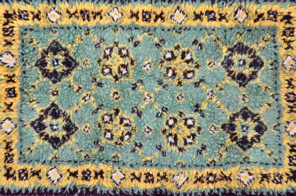 Green rug with yellow and black floral pattern and border.