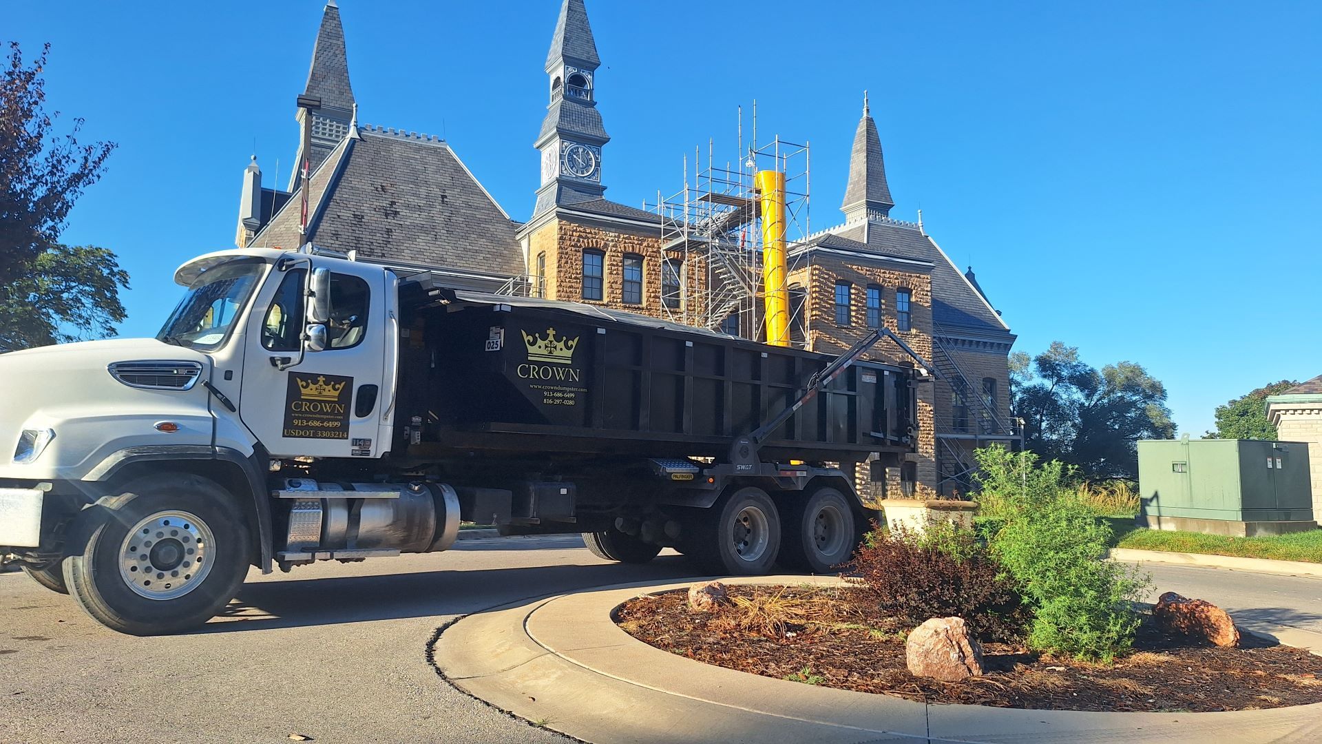 Dump truck parked in front of a stone building with spires and a landscaped roundabout.