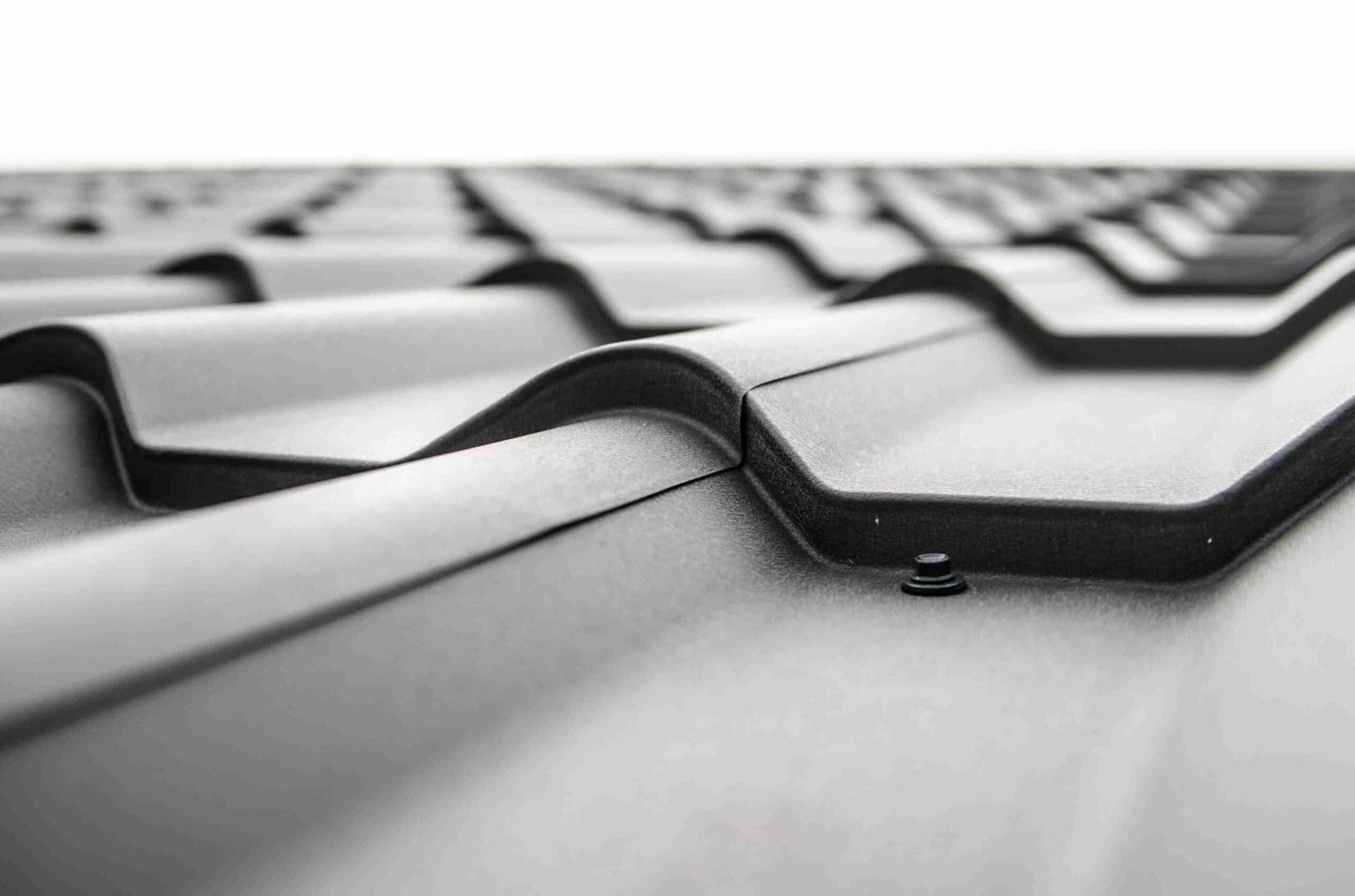 Close-up view of a dark metal roof with overlapping, wavy panels and fasteners.