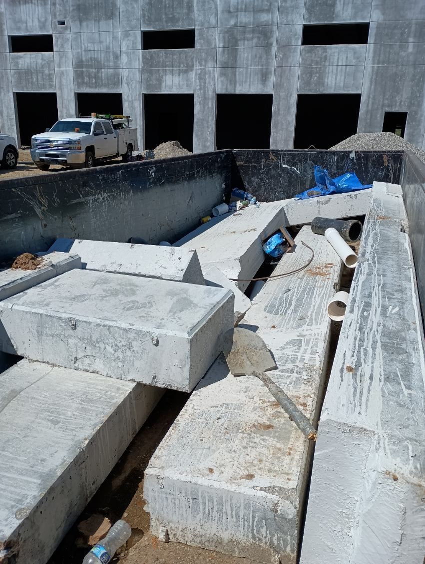 Concrete blocks piled in a large container at a construction site; building background.