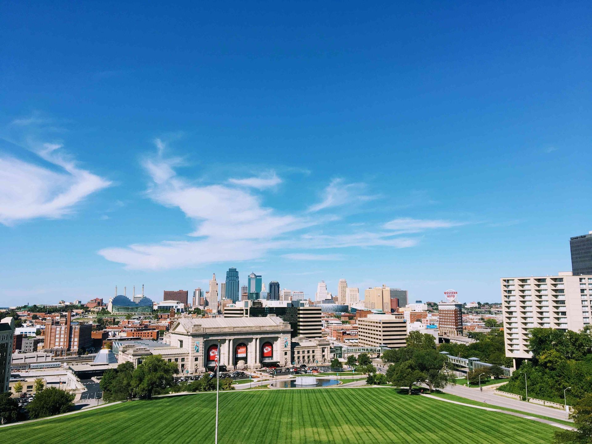 Kansas City, MO skyline on a sunny day. Large green lawn in foreground. Blue sky.